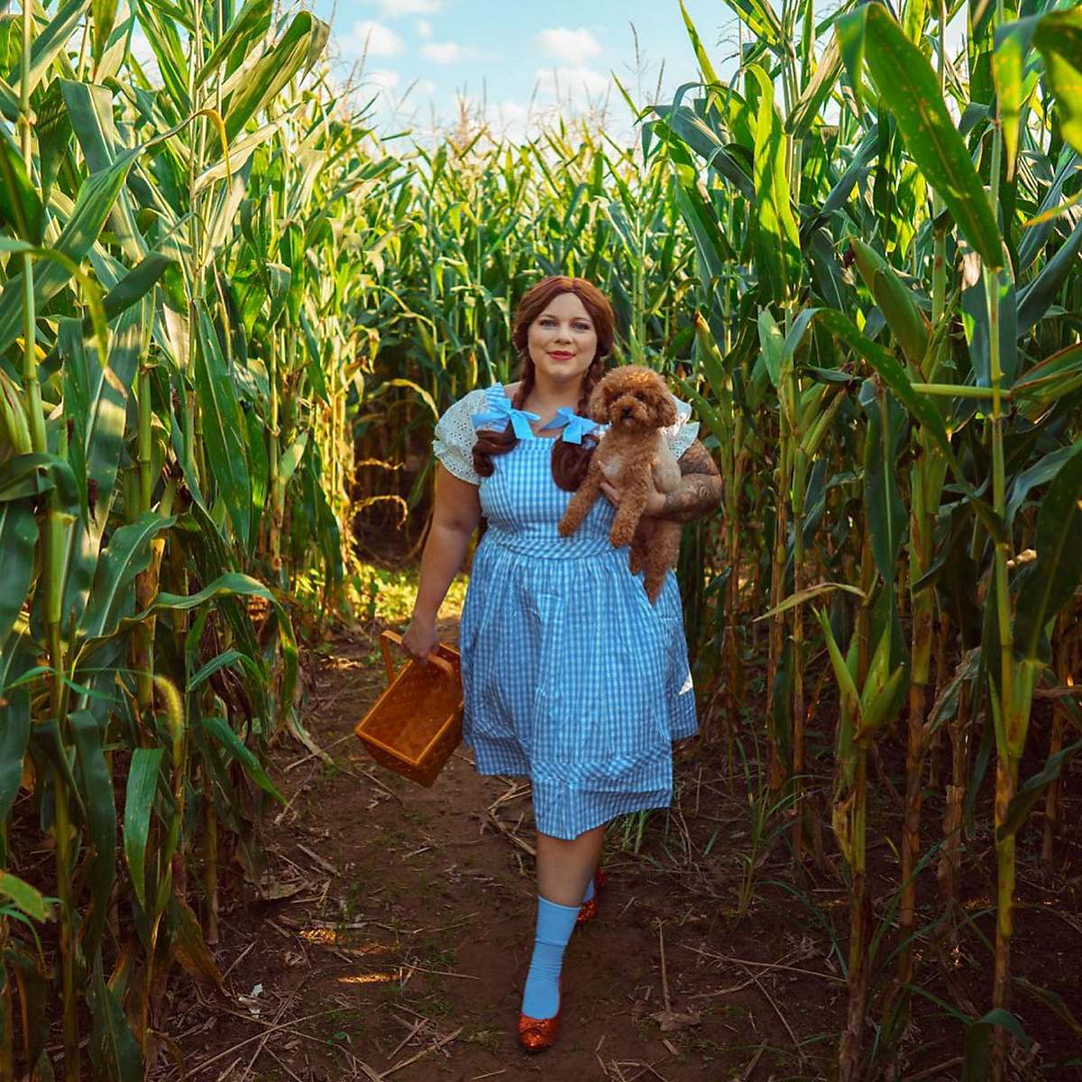 Woman in Dorothy from The Wizard of Oz costume holding Toto dog and basket
